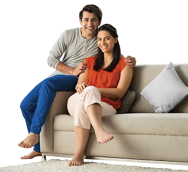 Couple sitting on sofa smiling against orange background.