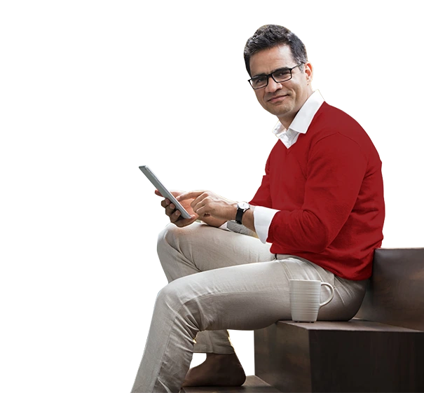A Man in a red sweater and glasses sits on stairs using a tablet, with a coffee mug beside him.