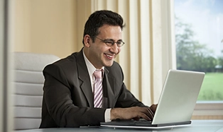 Businessman in suit smiling while working on laptop in office.