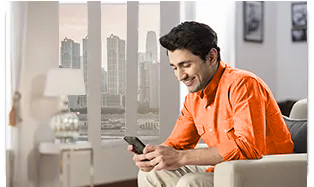 Man in orange shirt using smartphone while sitting on sofa at home.