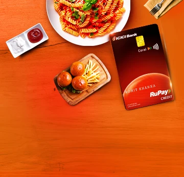 ICICI Bank Coral RuPay credit card on a wooden table next to food. Text: The card you need is right here.