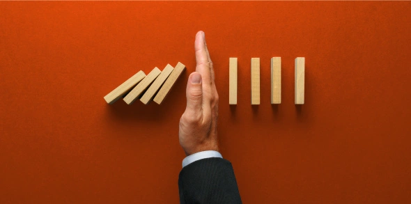 Hand stopping falling dominoes on red background.