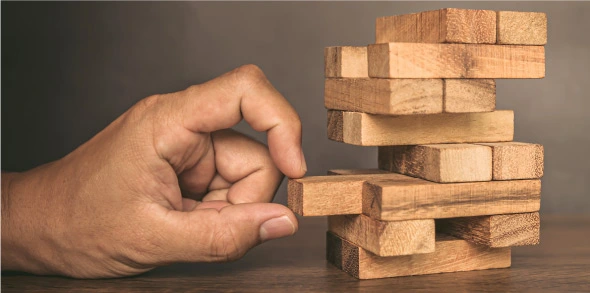 Hand removing wooden block from stacked tower, risk concept.