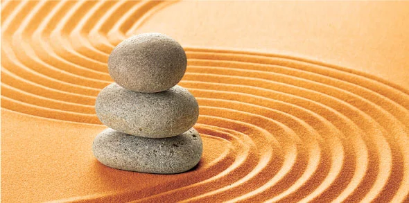 Three stacked stones on sand with circular ripple patterns symbolizing balance.